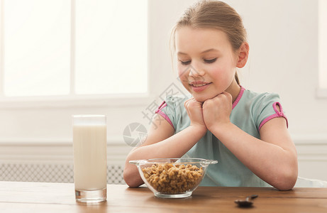 快乐的小女孩坐在餐桌旁看着玻璃杯中的谷物和牛奶图片