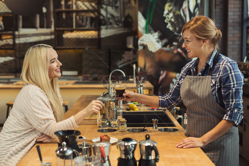 微笑的咖啡师从顾客那里拿信用卡在咖啡店柜台买饮料小企业职业人员支付和服务理图片