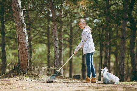 年轻微笑美丽的女人在公园或森林的垃圾袋附近清洁和使用耙子收集垃圾环境污染问题停止自然垃背景图片