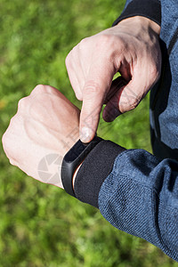 男士手上的健身手镯或智能手表以绿草为背景一名身着蓝带的成年男健康的图片