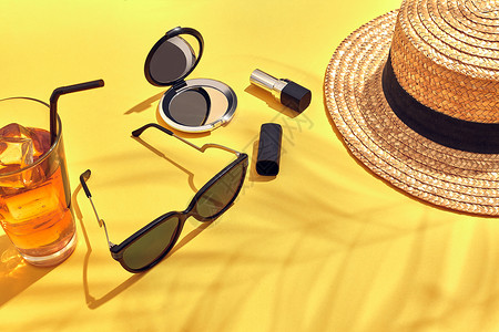 草滩妇女帽子杯中冰的饮料和黄色背面的太阳镜背景图片