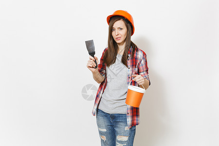 年轻有关妇女在保护建筑橙色头盔拿着油漆桶和油灰刀隔离在白色背景图片