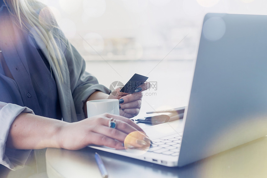 关闭了女手拿着信用卡和在键盘上打字的视图一位女商人坐在咖啡店里通过笔记本电脑图片