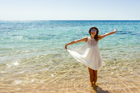 年轻女子穿着白色的裙子和帽子站在海滩上图片