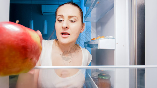 饥饿的年轻女在晚上冰箱里找吃的近身照片图片