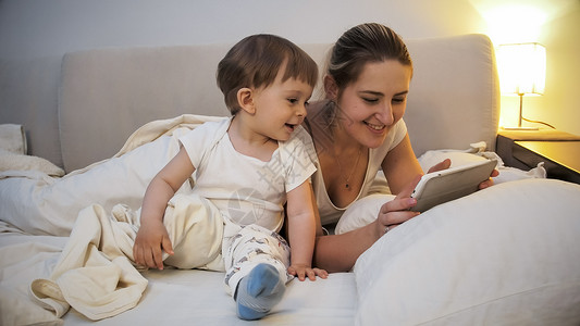 睡前使用数字平板电脑穿着睡衣的快乐母亲图片