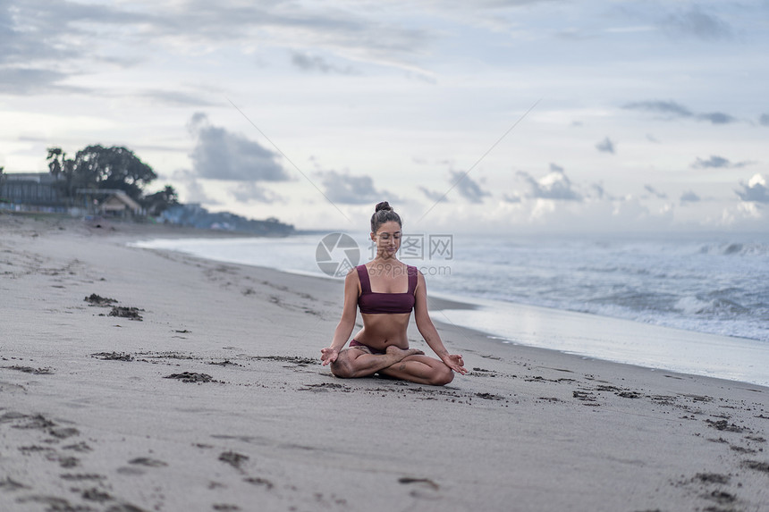 有吸引力的年轻女子在露珠padmasana上与海边青图片