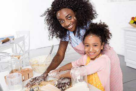 美国母亲和女儿微笑的非洲母亲和女儿一起在厨房里敲图片