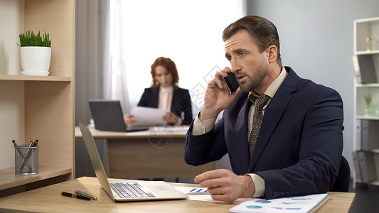 男用笔记本电脑在办公台打字接听移动电话客户护图片