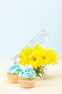 带有蓝色奶油装饰和柔背景玻璃中的黄色菊花束的纸杯蛋糕图片