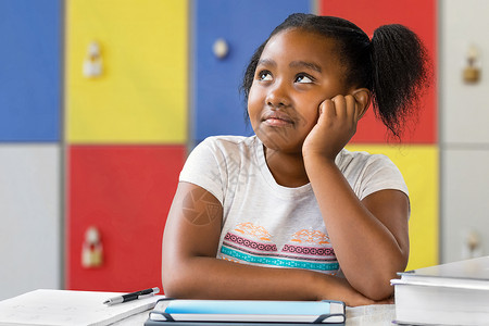 坐在教室桌前的小非洲女学生的近距离肖像令人厌烦地想着面部表情盯着望图片