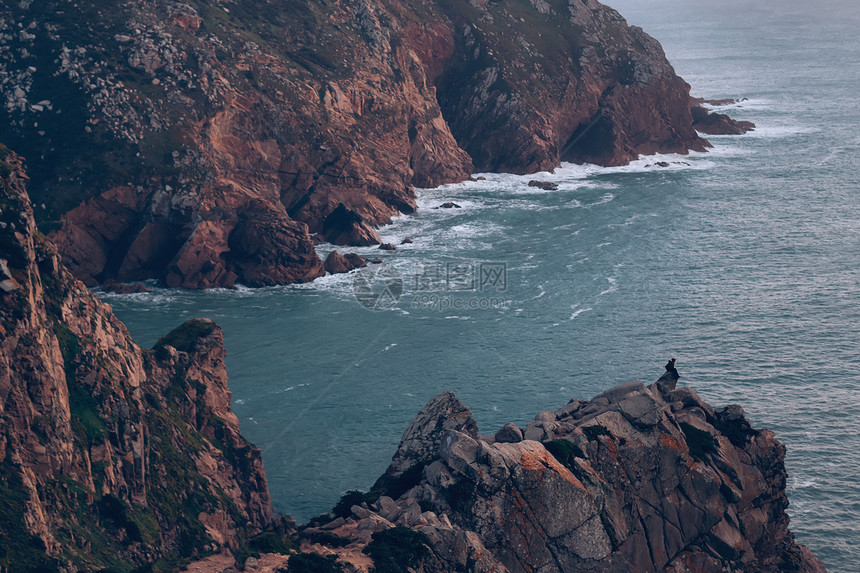 岩石山丘和独自游客坐在边缘享受海洋图片