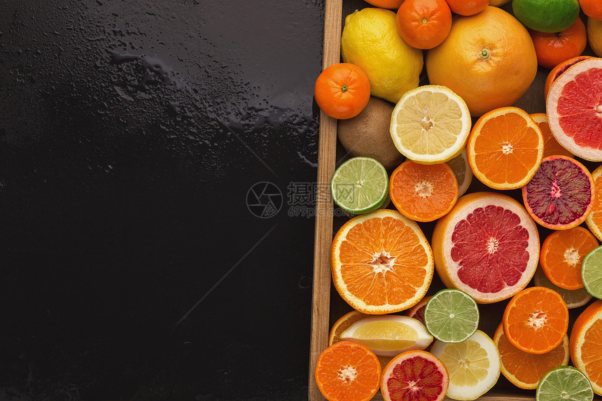 在湿黑色背景上装有各种柑橘的盒子图片
