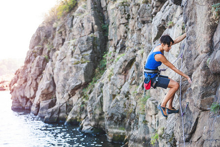 水面上的登山者一个女人爬上岩石自然地形训练极限运动在海图片
