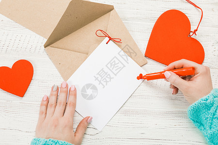 在圣情人节写情书的女孩之手与红色心形图的手工制作的明信片2月14日节庆典带有复制空间背景图片