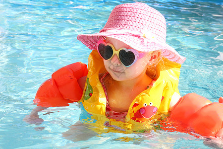 一个2岁的幼儿女孩在游泳池里带着手臂浮筒和安全救生背心在阳光明媚图片