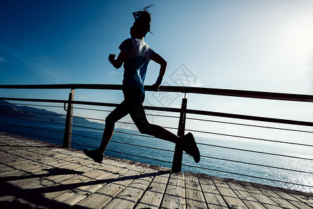 日出时在海边木板路上奔跑的运动健身女跑者图片