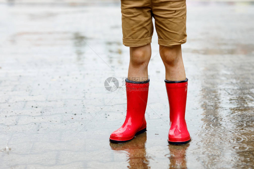 穿着红色雨靴的孩子跳进水坑特写孩子玩得开心泼水温暖的夏雨图片
