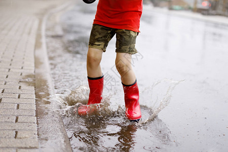 穿着红色雨靴的孩子跳进水坑特写孩子玩得开心泼水温暖的夏雨图片