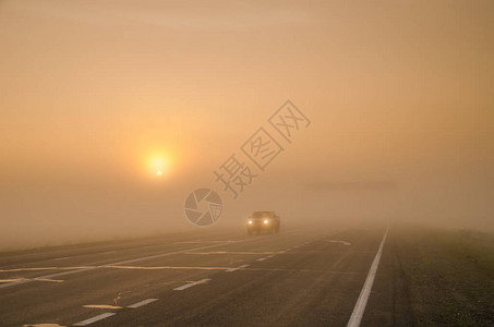 车前灯光照亮了在城市外面雾中沿路行图片