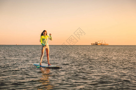 在日落时在热带海洋水上冲浪板上身着时装运动服饰的图片