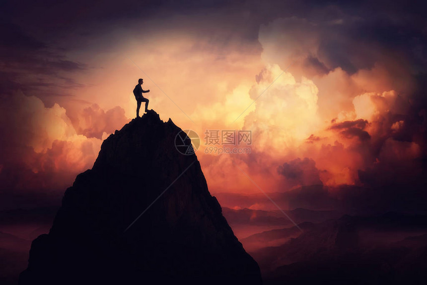 自我克服概念作为一个商人在云层上攀登一座高山在日落背景下赢得和成功的道路实图片