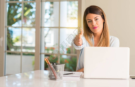 在家里拿着笔记本电脑坐桌的女学生举起手来欢迎以握手相亲表示信任和成图片