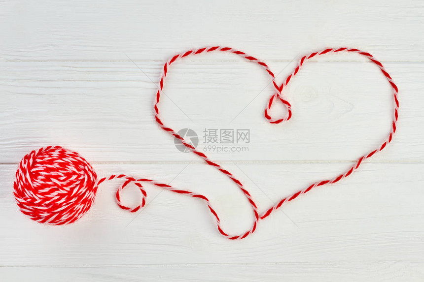 从红色羊毛线的心形状心由白色木制背景上的红色羊毛纱制成用于在木制背景上编织的毛球图片