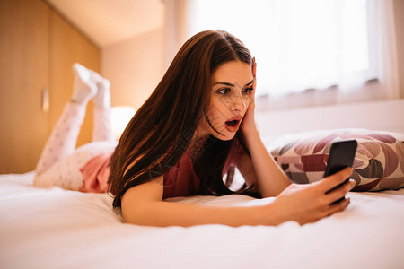 女孩在家躺在床上时在看电话图片