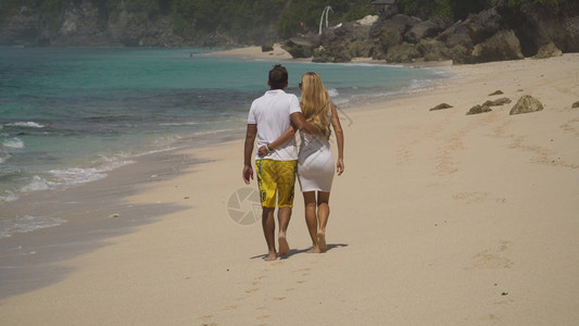 美丽的情侣拥抱沿着海滩散步图片