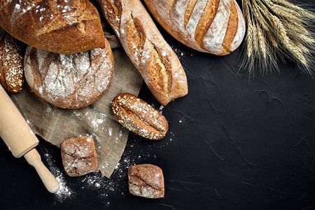面包店黑色板背景上的质朴硬皮面包和小圆面包静物从顶视背景图片