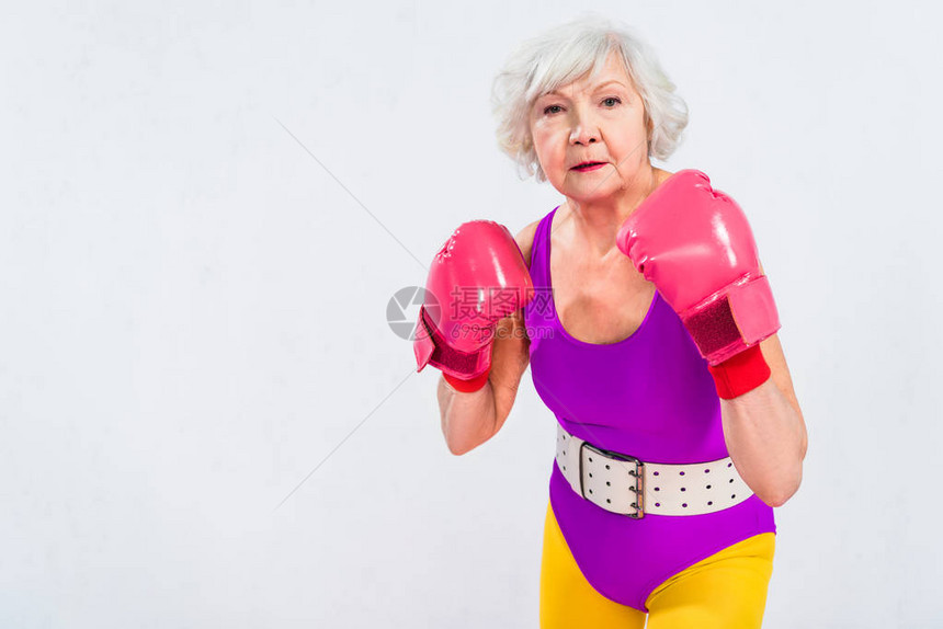 身穿运动服和拳击手套的高级妇女看着在灰色上图片