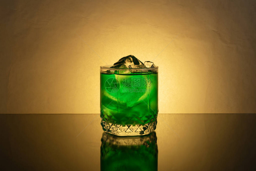 一杯有绿色薄荷饮料的杯子和一小块粉碎的冰块在反光图片