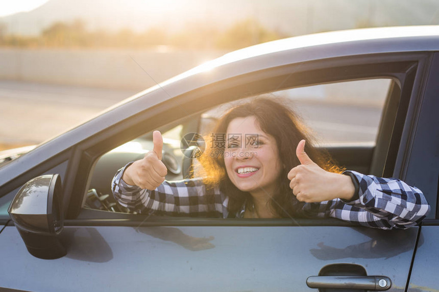 女司机开心地笑着竖起大拇指从停车场外面的蓝色汽车侧窗里出来美丽的年轻女子对她的新车感到满意图片