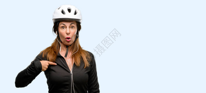 使用耳机的中年骑自行车妇女欢乐和惊讶地欢呼着表达Wow手势图片