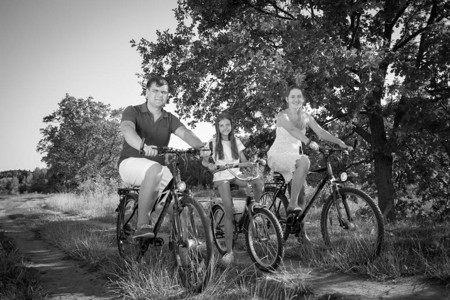 双亲在公园中骑着自行车与女儿一起乘自行车的快图片