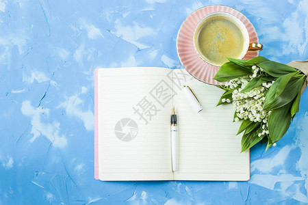 一束山谷百合花一杯咖啡和一张笔记本放在蓝桌子上清晨春光图片