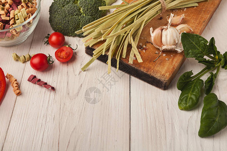 白色木桌上的生手工绿色意大利面条配菠菜汁西兰花西红柿大蒜和香料烹饪意大利面背背景图片