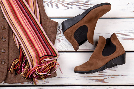 女时尚棕色踝靴女羊毛背心五颜六色的围巾和鞋子木制背景上的图片
