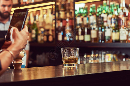 酒吧顾客的剪裁图像在电话中拍摄了酒吧柜台酒杯的照片笑声图片