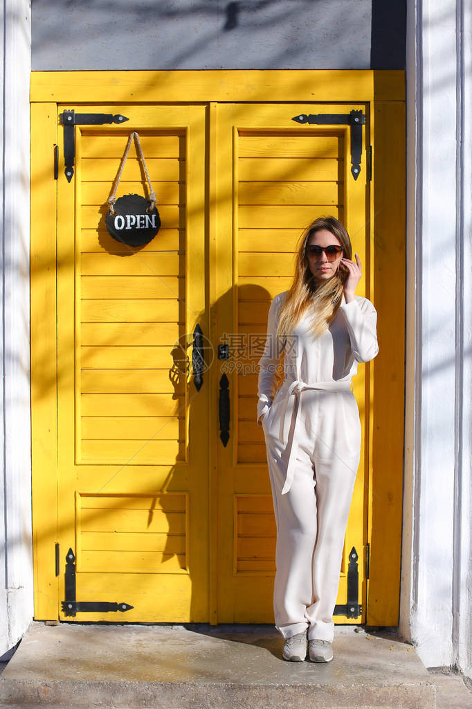 身着白色西装和眼镜的金发美国女人站在咖啡馆门边图片