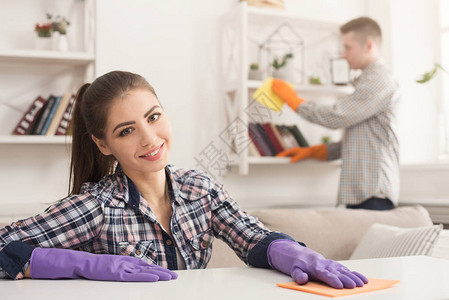 年轻夫妇在橡胶手套式清洁房用毛巾擦灰在客厅复制空间洗刷粉尘图片