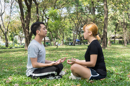 年轻的情侣在下午在温暖的阳光下在公园环抱中锻炼后冥想以平息心情瑜伽运动和健康生活方式的概念情侣背景图片