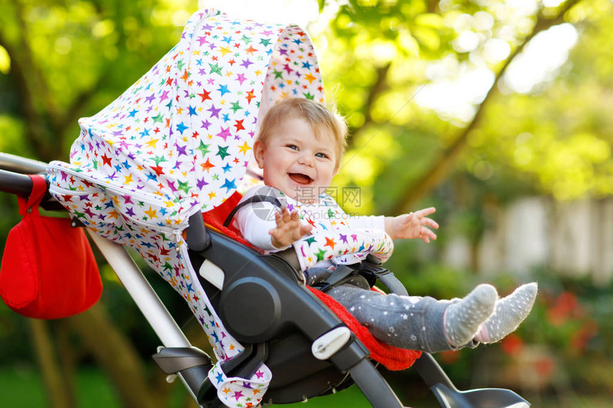 可爱的小漂亮女婴坐在婴儿车或婴儿车里等妈蓝眼睛的快乐微笑的孩子有绿树背景宝图片