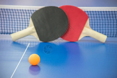 乒乓球的橙色球和两个红色和黑色的木制球拍图片