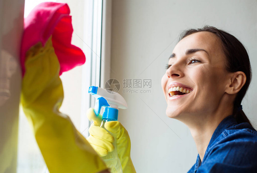 美丽的年轻女子在清扫房屋窗户时使用喷图片