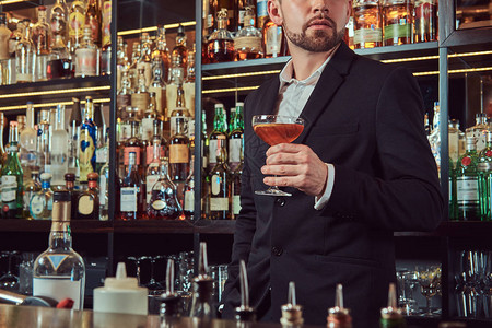 卡萨诺瓦英俊的时尚男子在酒吧柜台背景中拿着一杯背景