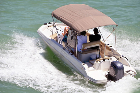 舵手和两名乘客在佛罗里达州迈阿密海滩附近的佛罗里达内陆水道上乘坐由单个舷外发动机驱动的小型摩托艇背景图片