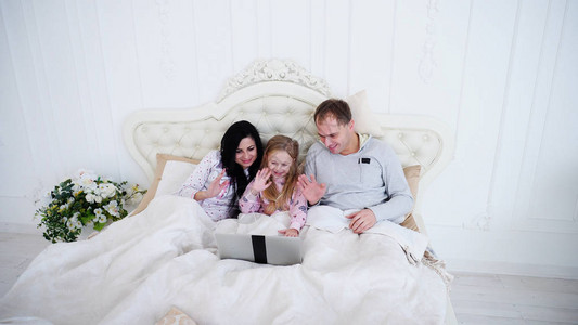 小漂亮女儿和父母在床上用笔记本电脑现代科技的概念还有周末早图片