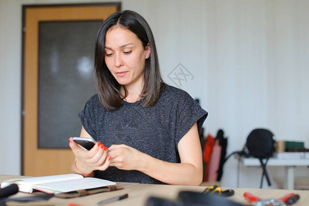 欧洲妇女使用手机为带有黑色皮革的手工笔记本拍照手工业皮革工业和家图片